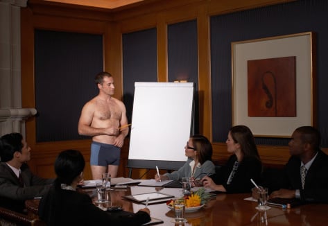 Picture of a woefully underdressed gentleman pointing to a blank flipchart in board room full of suits